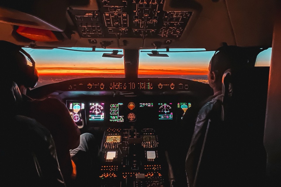 Two pilots at the controls of an airliner flight deck at dusk
